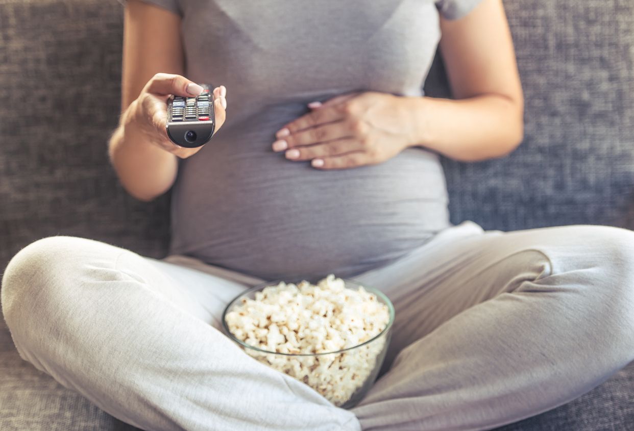 Dona embarassada que mira una pel·lícula amb crispetes des del sofa