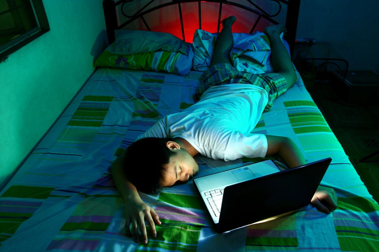 Un nen dormit sobre un llit, davant un ordinador