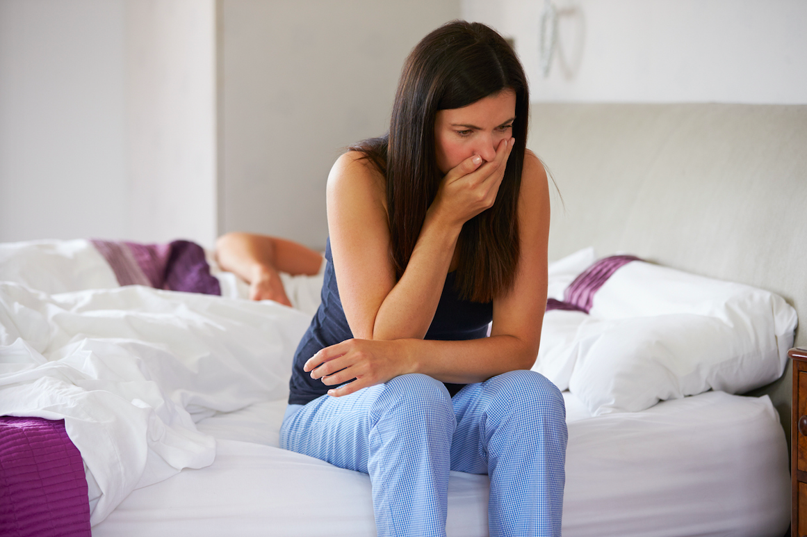 Una noia sentada en un llit de matrimoni i amb pijama amb ganes de vomitar